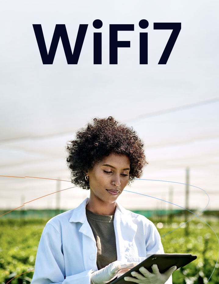 A woman scientist in a white labcoat looking at an ipad in the foreground with a field in the background.